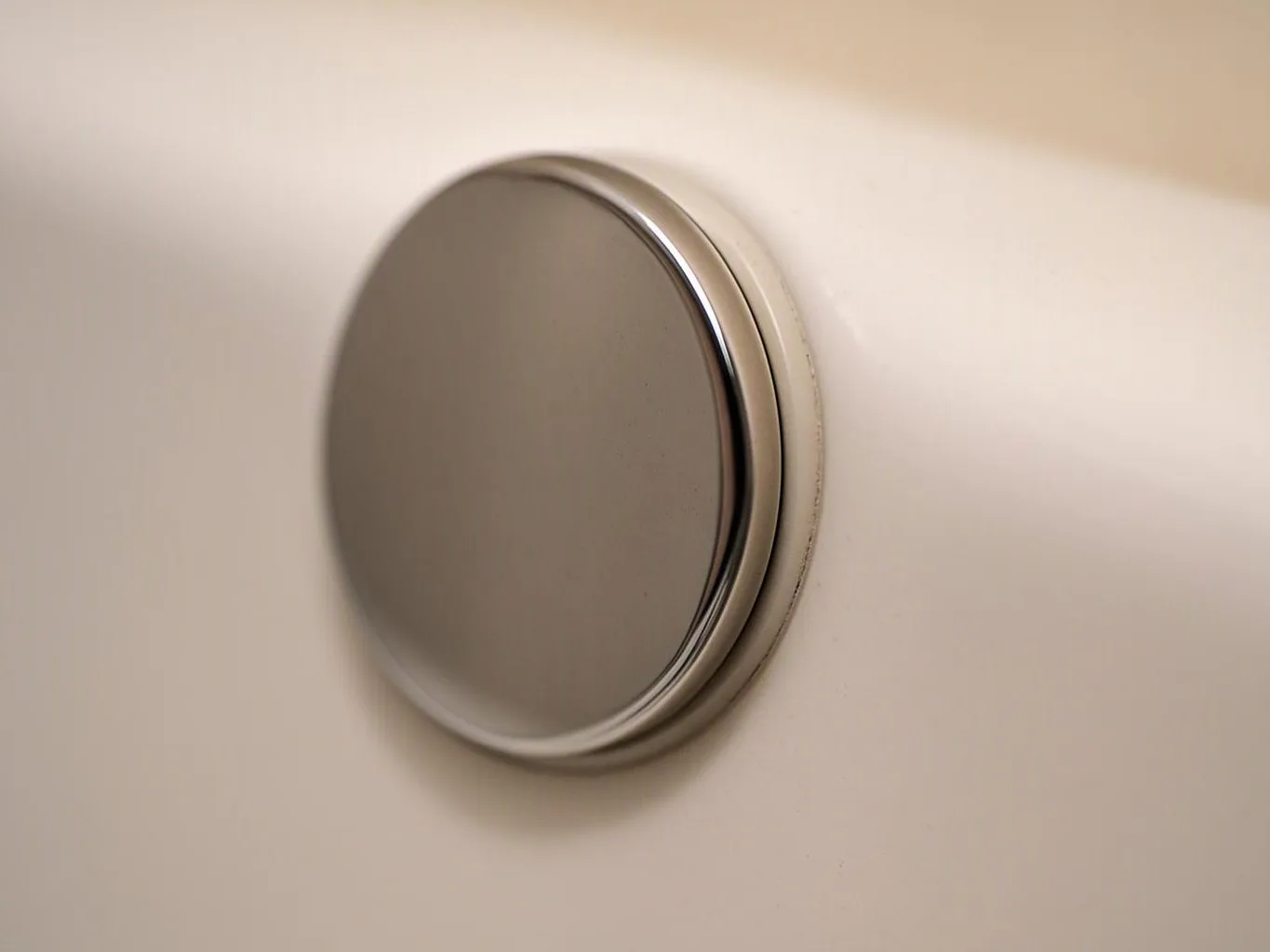 A round silver button or drain cap sits flush against a white wall or surface